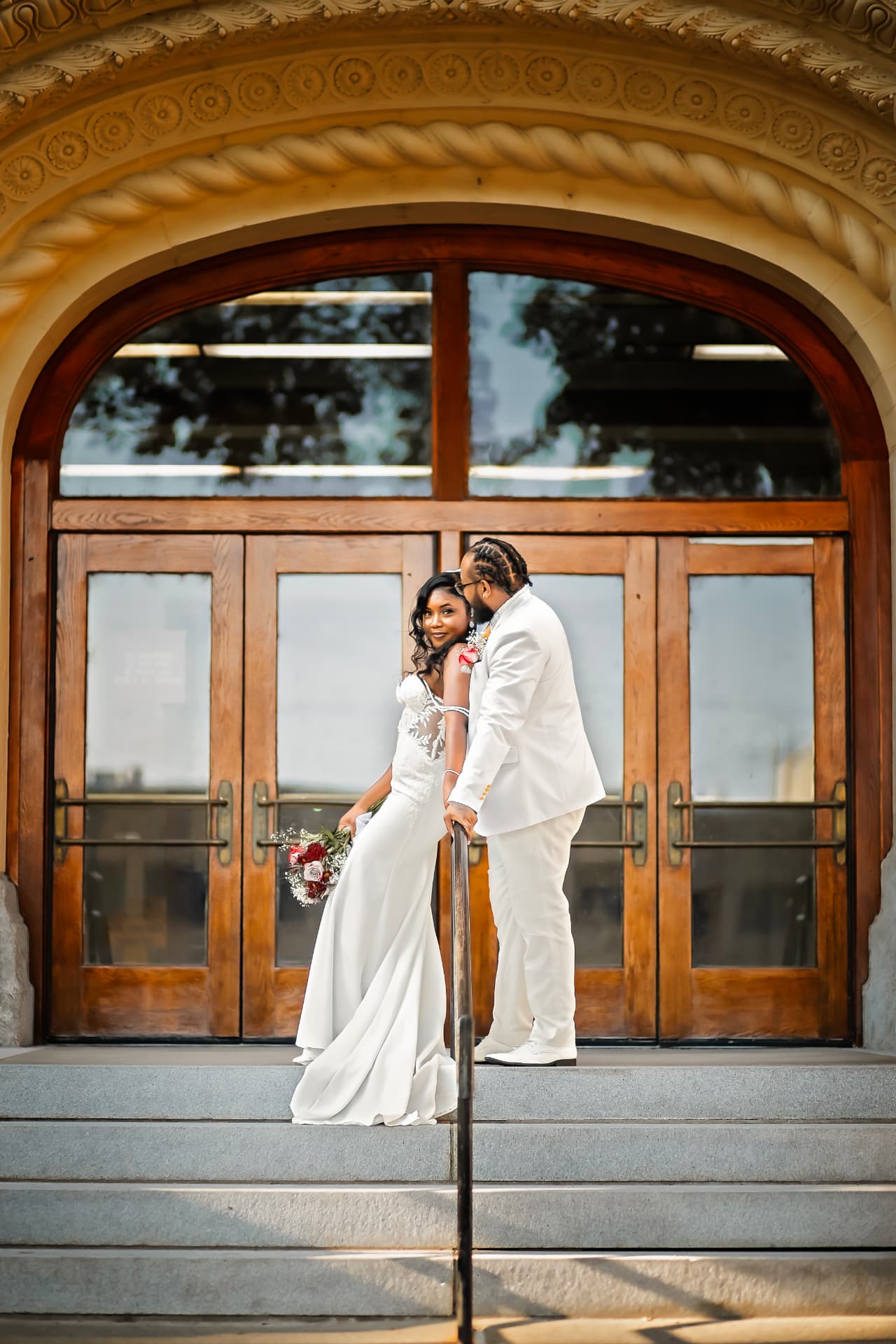Bride and groom on the steps of a grand theater entrance, looking back at the camera