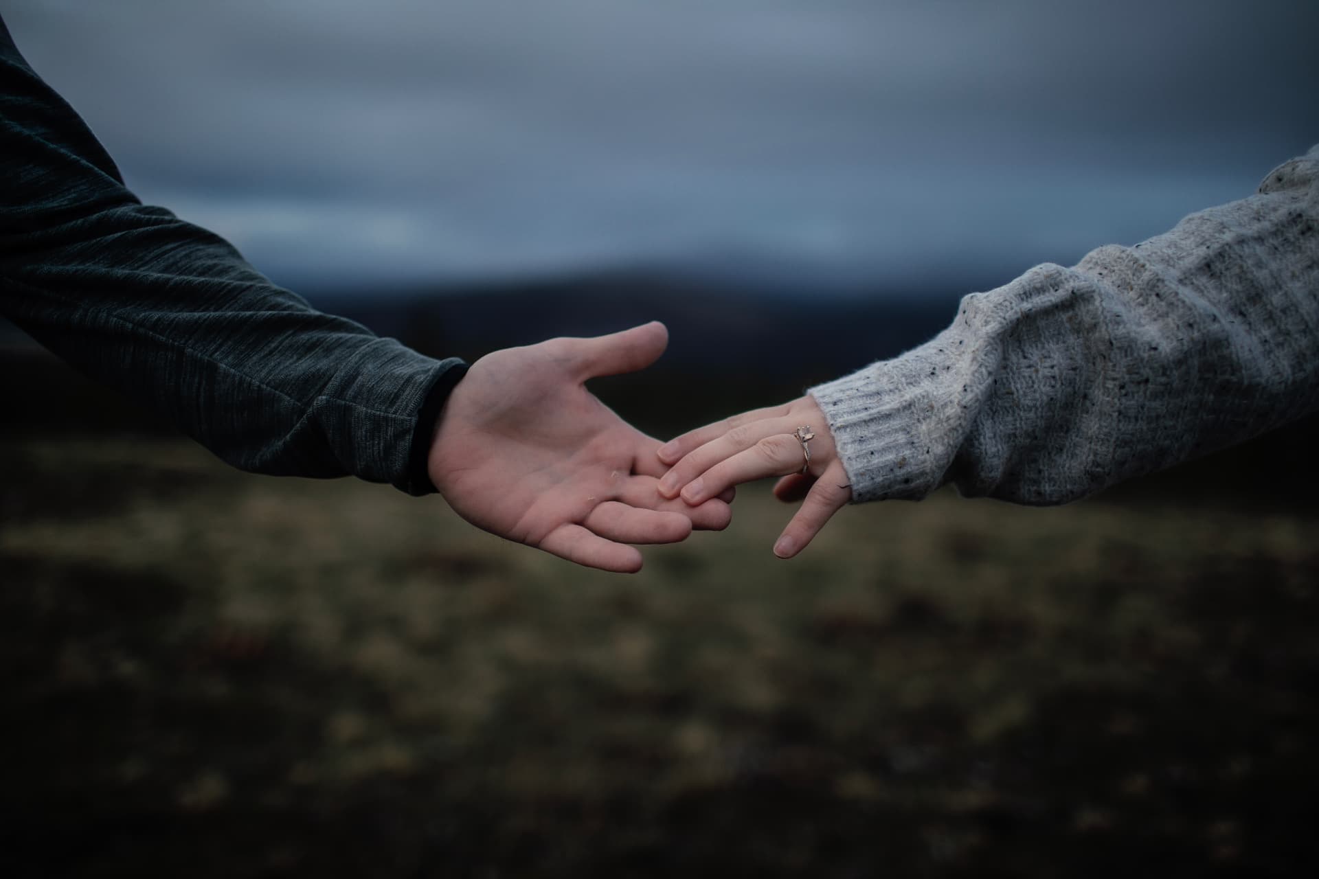 Couple reaching for each other's hands, engagement ring out, under a moody sky