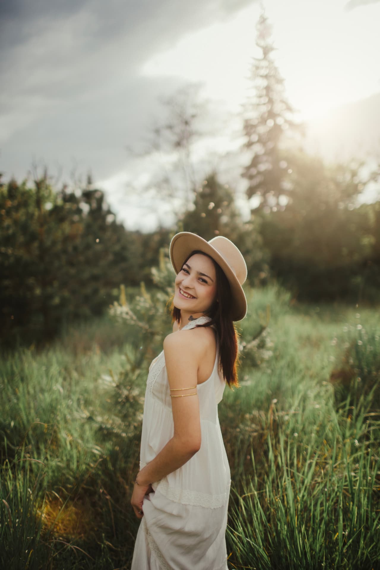 Smiling senior in a hat and white dress in a sunlit meadow