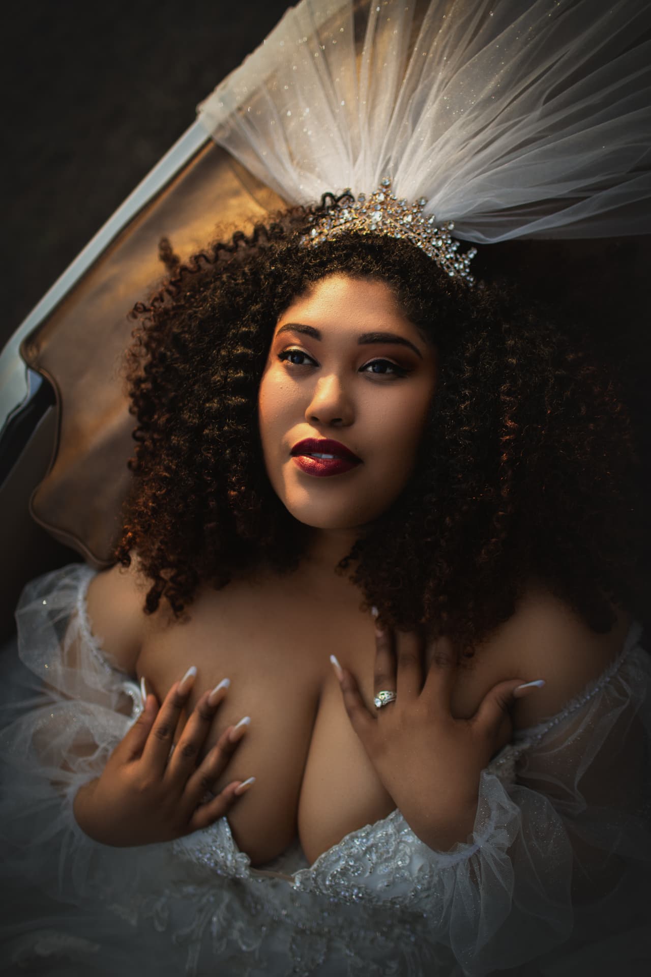 Bridal portrait with a dramatic fanned veil and jeweled crown over a vintage car