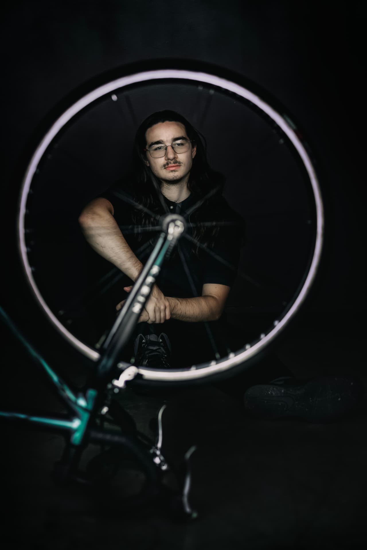 Senior with long hair framed through a bicycle wheel in a dark studio