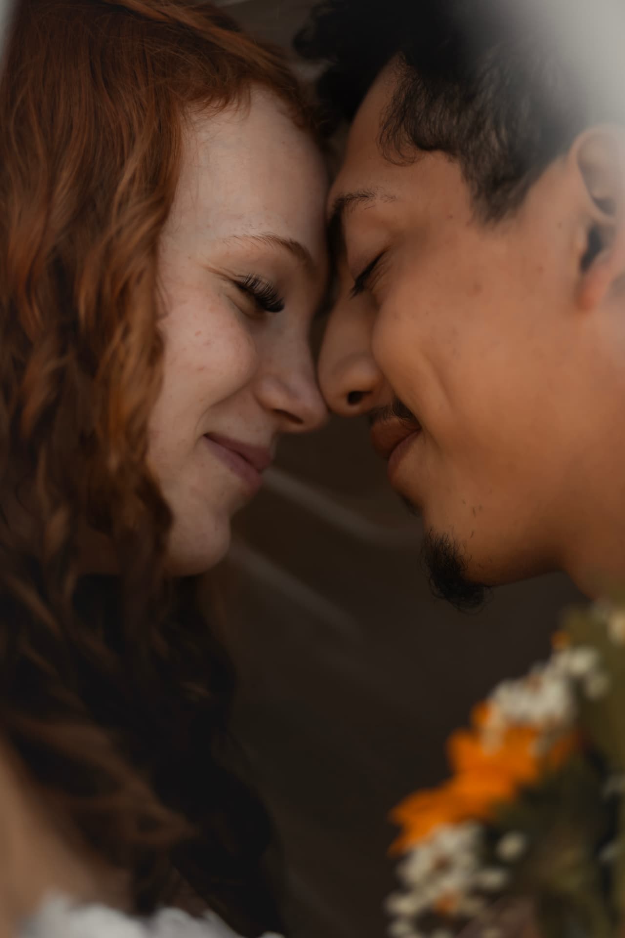 Bride and groom forehead to forehead in soft window light, eyes closed and smiling