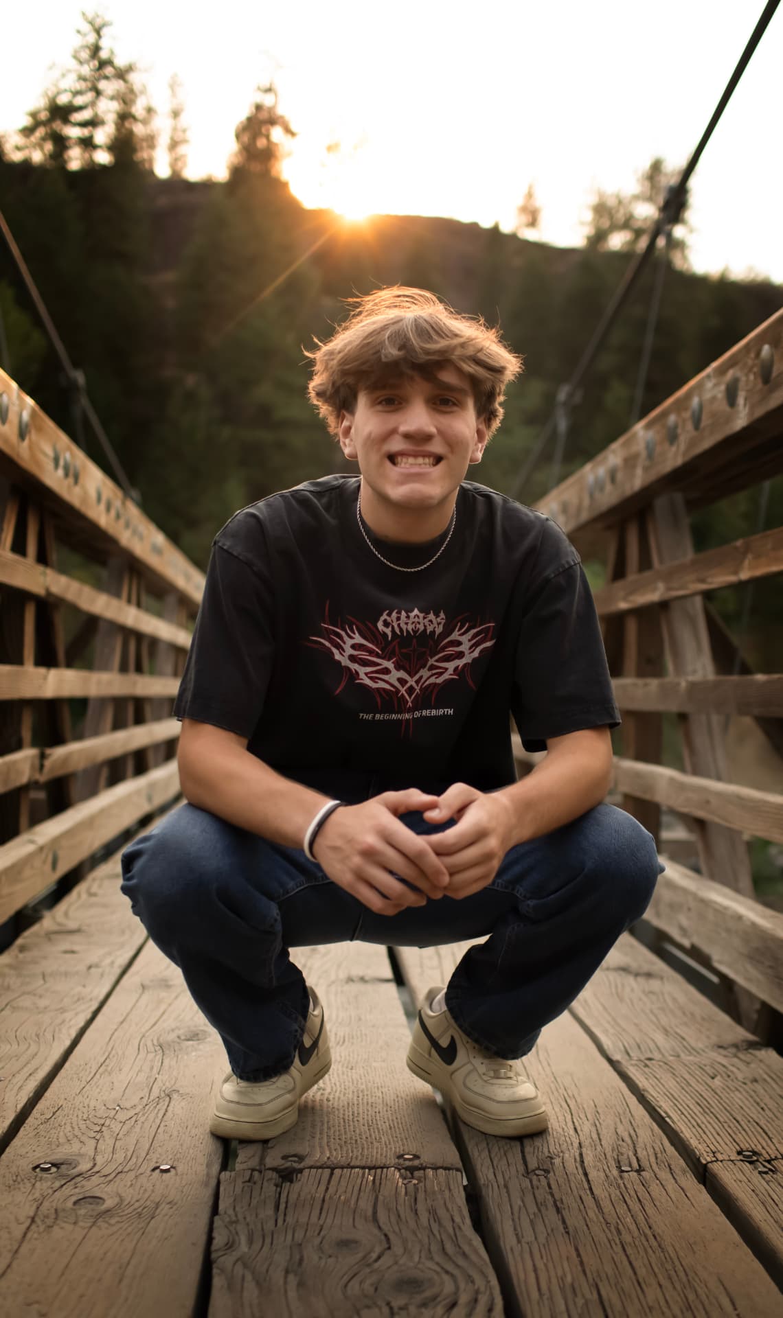 Smiling senior crouching on a wooden bridge at sunset