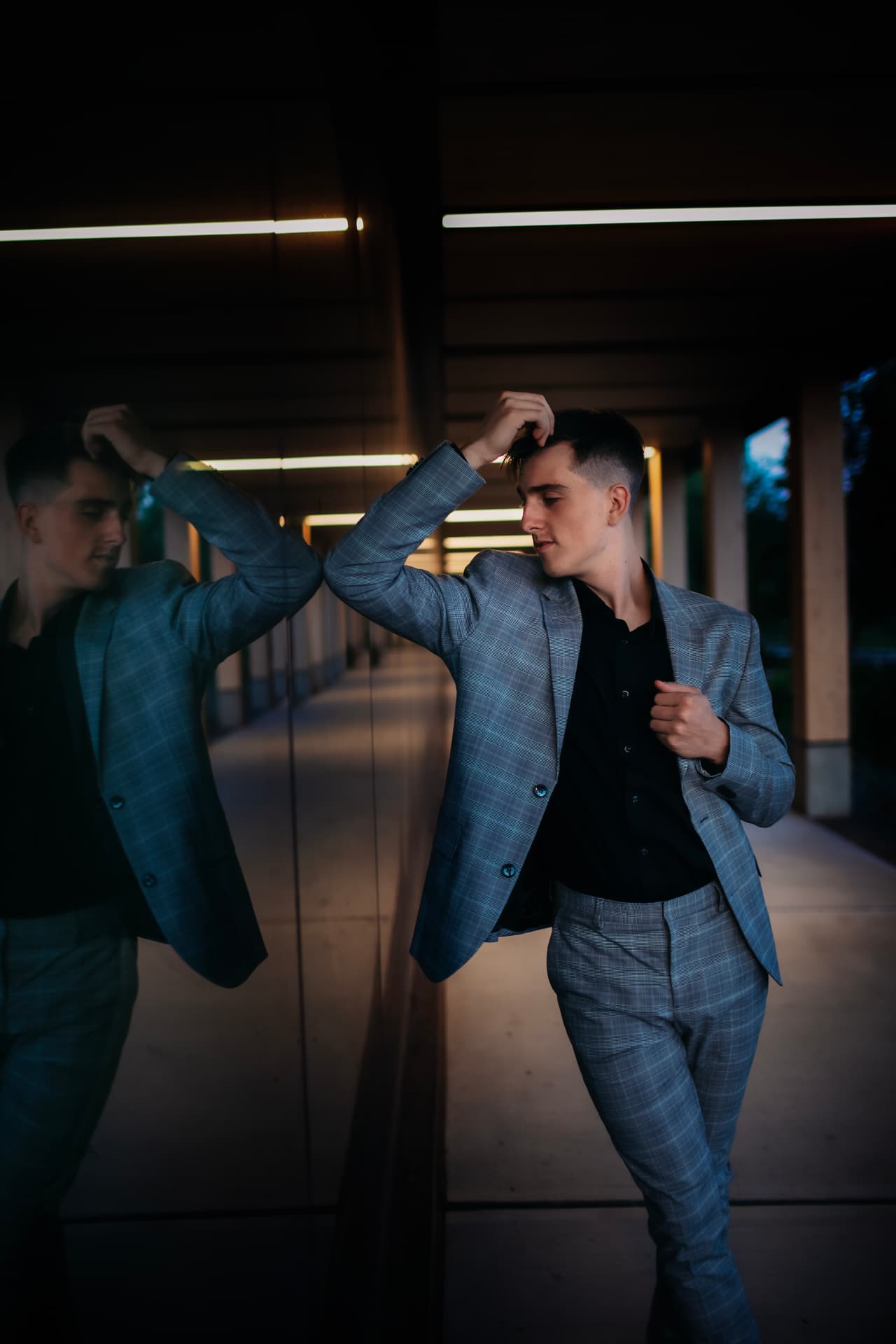 Senior in a gray plaid suit posing against a mirror at dusk