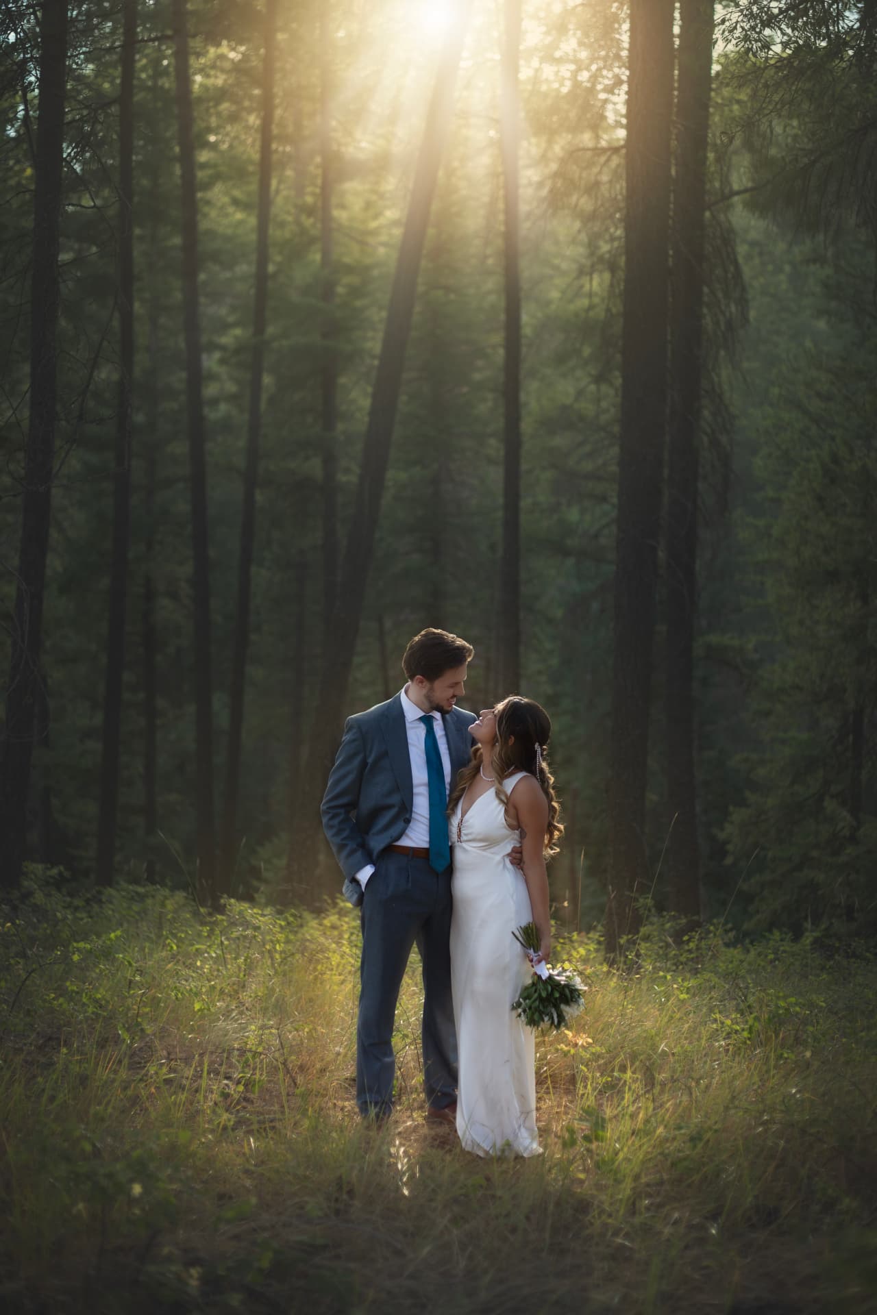 Bride and groom standing face to face in a sunlit pine forest