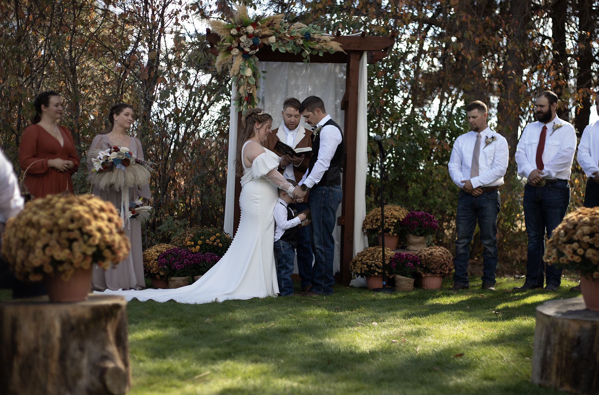 Bride and groom exchanging vows with their son at an outdoor autumn ceremony
