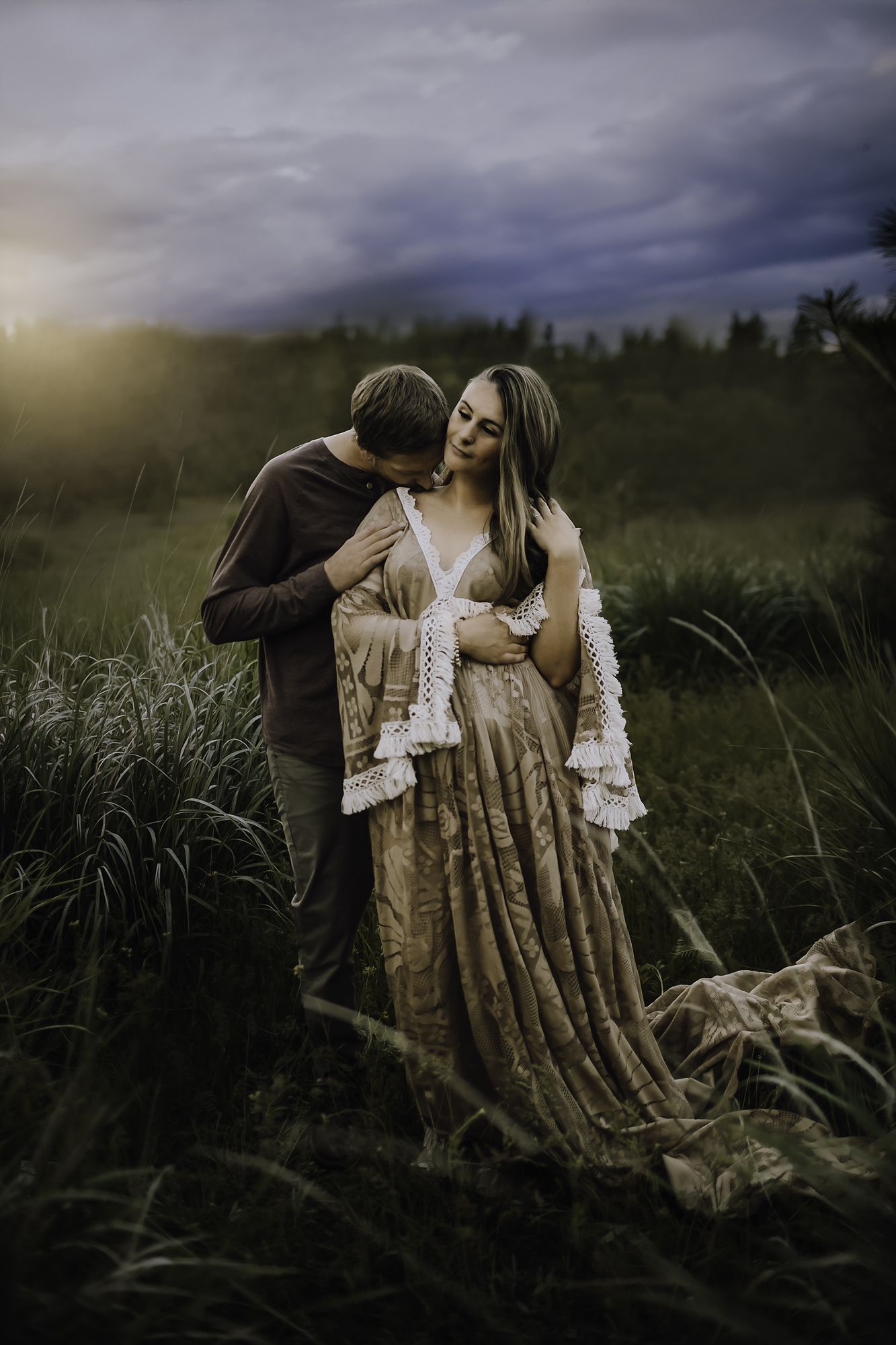 Couple embracing in a tall grass field under a dramatic dusk sky
