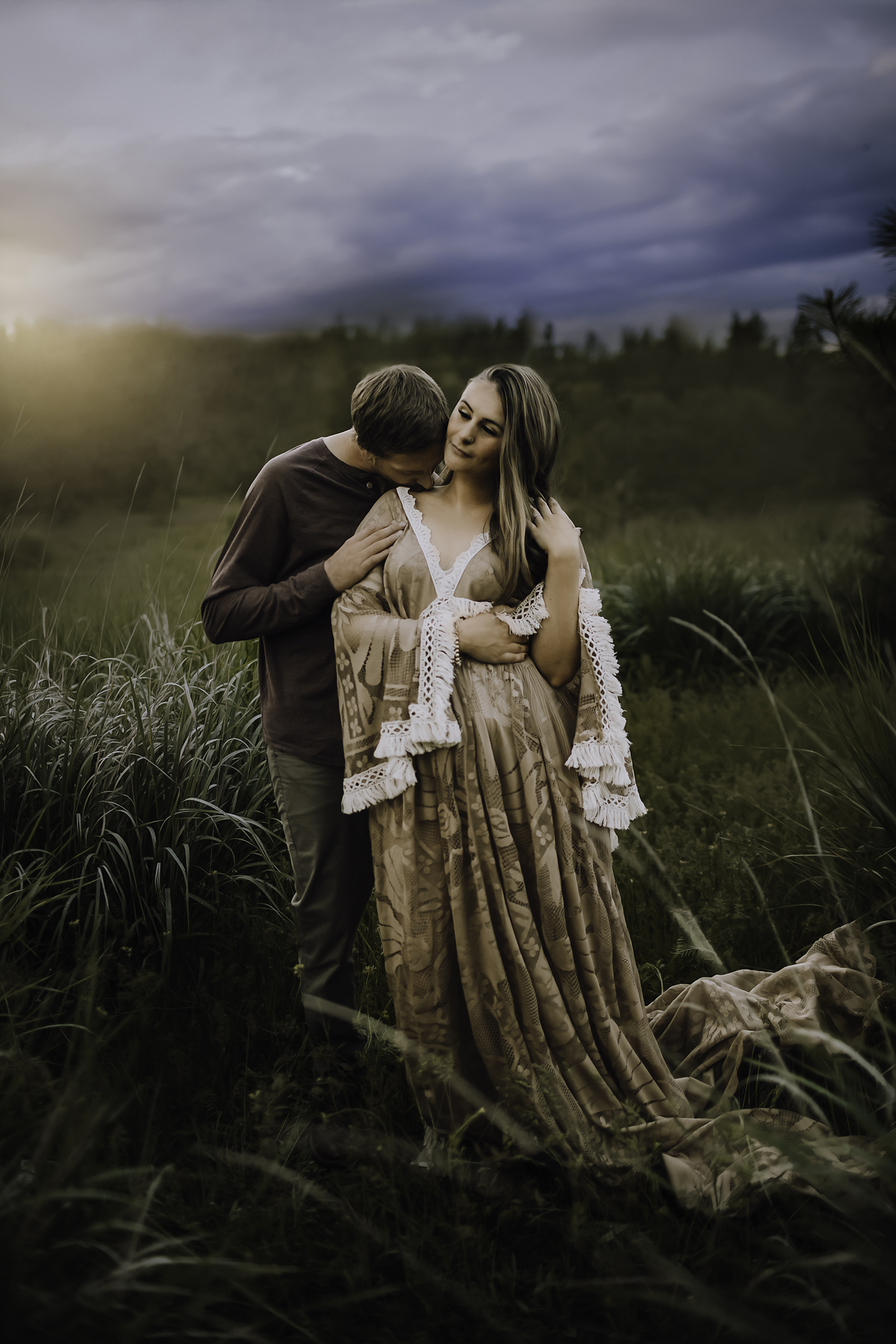 Couple embracing in a tall grass field under a dramatic dusk sky