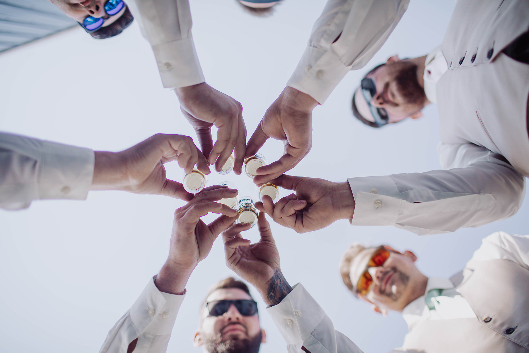 Groomsmen toasting together from below against the sky